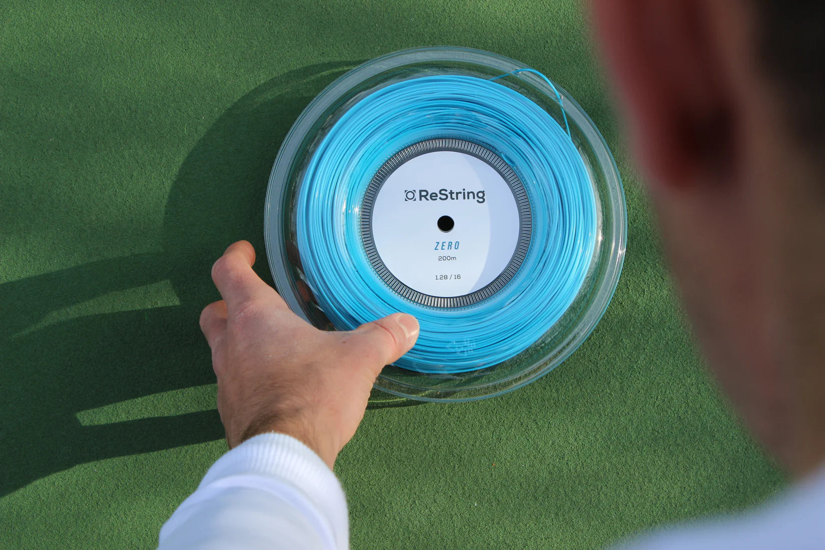 hand picking up a reel of restring zero strings in blue on a green background