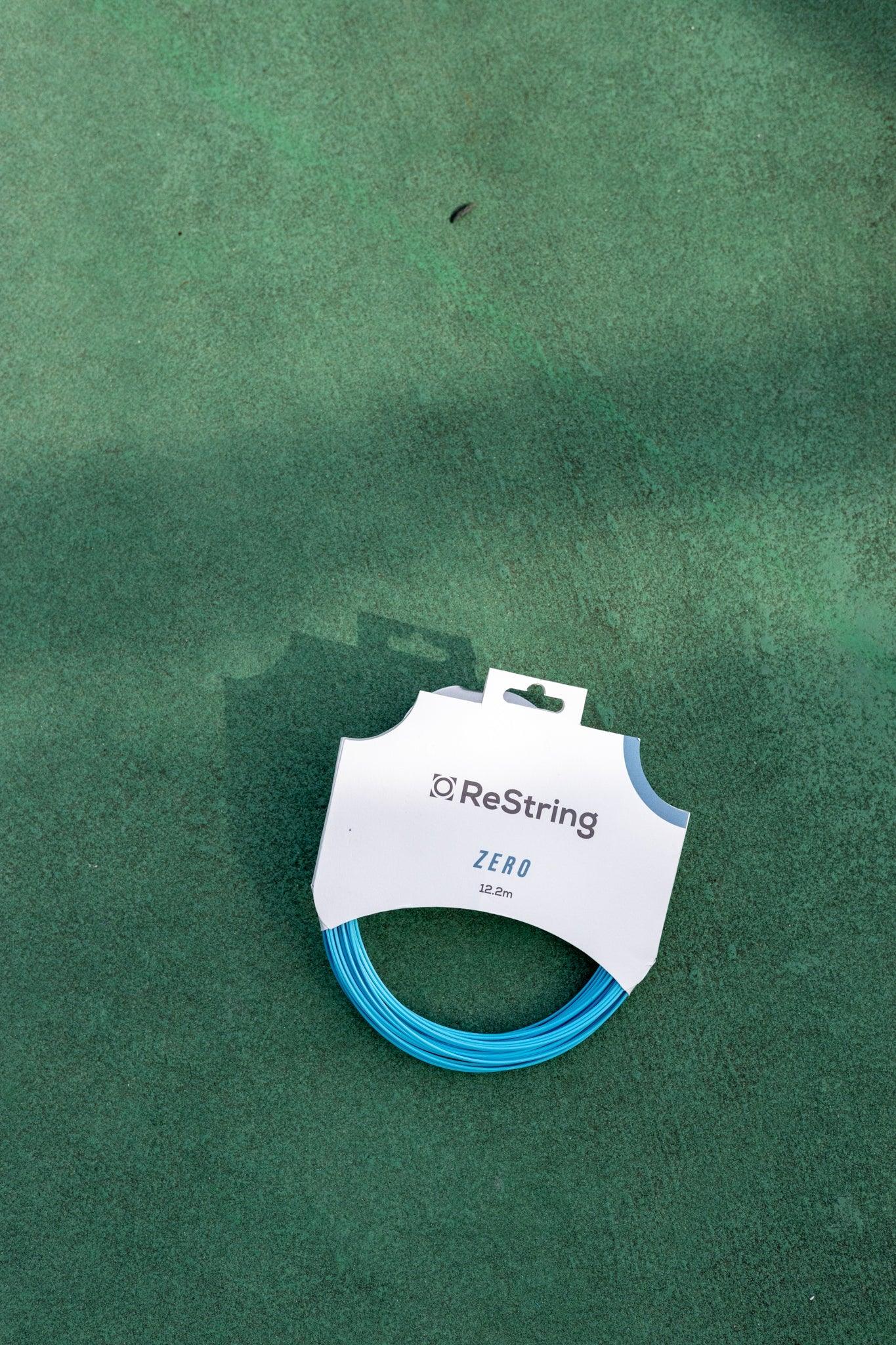 a set of restring zero tennis strings in blue on a green tennis court