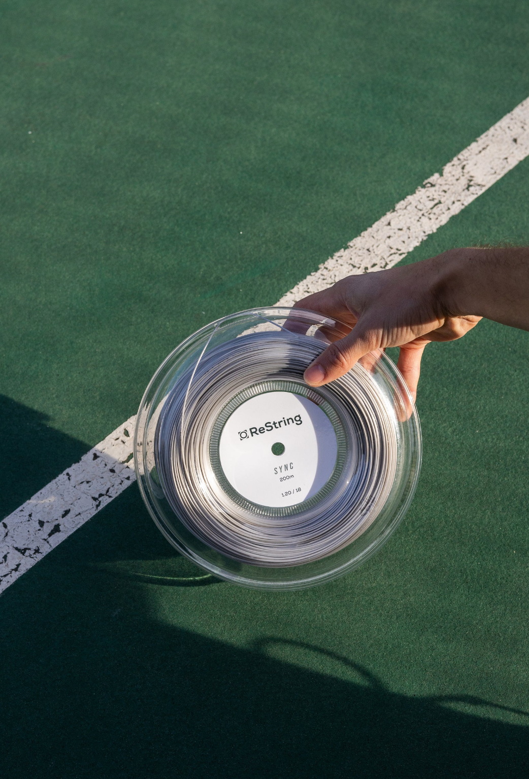 guy holding restring sync reel tennis strings on a green tennis court