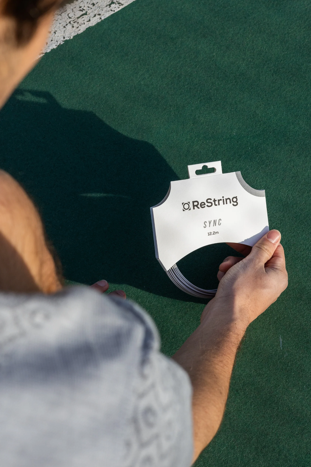 a man holding a pack of restring sync on a tennis court