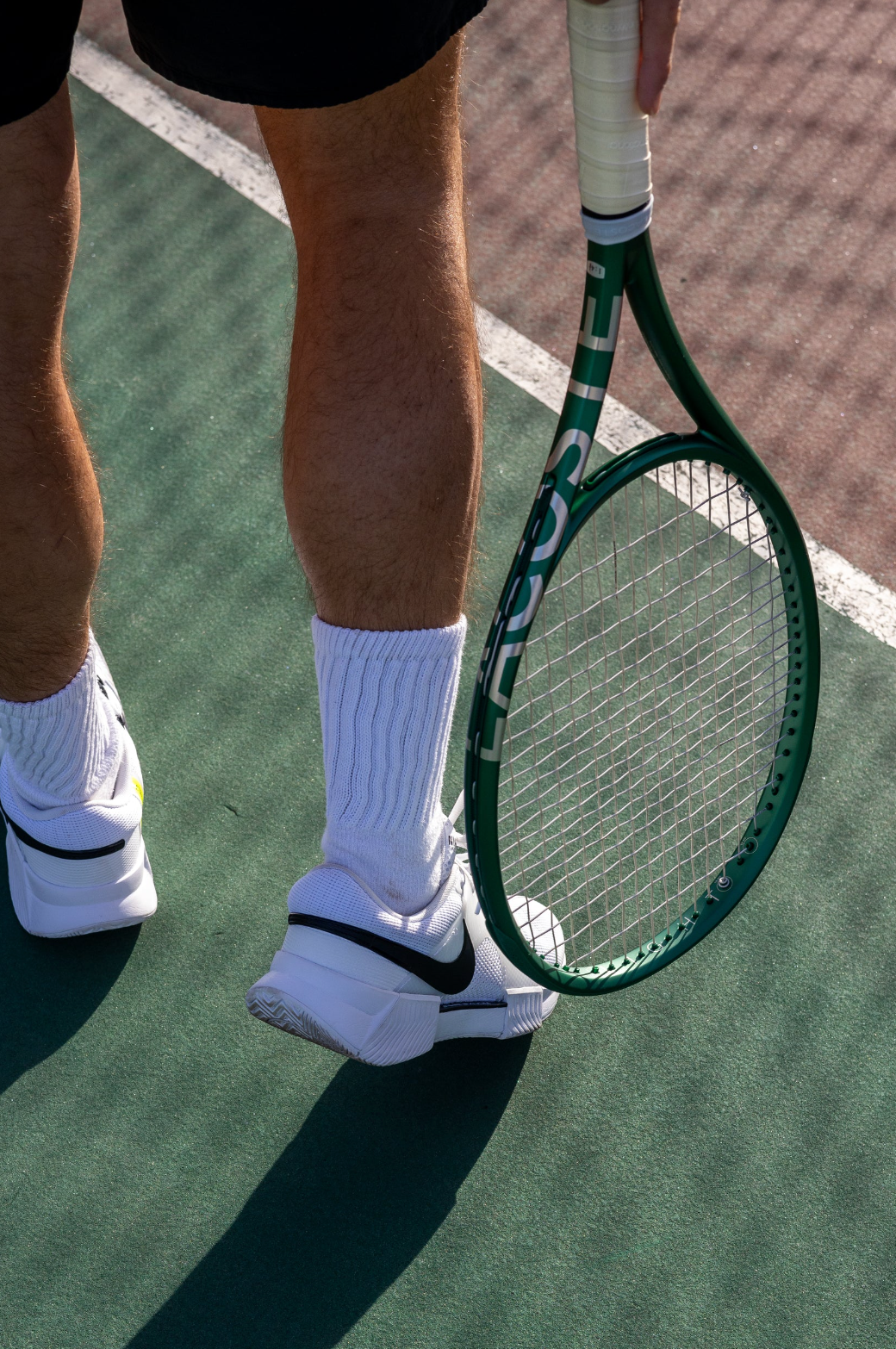 a man holding a lacoste racquet on a tennis court wearing nike shoes